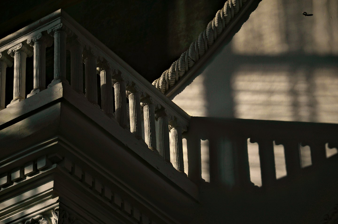 White fluted staircase balustrade casting geometric shadows on a wall.